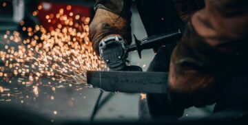 Worker uses a handheld grinder, sending sparks across a metal surface