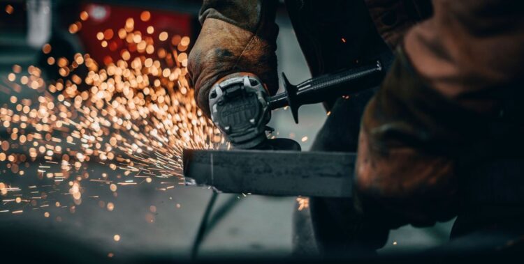 Worker uses a handheld grinder, sending sparks across a metal surface